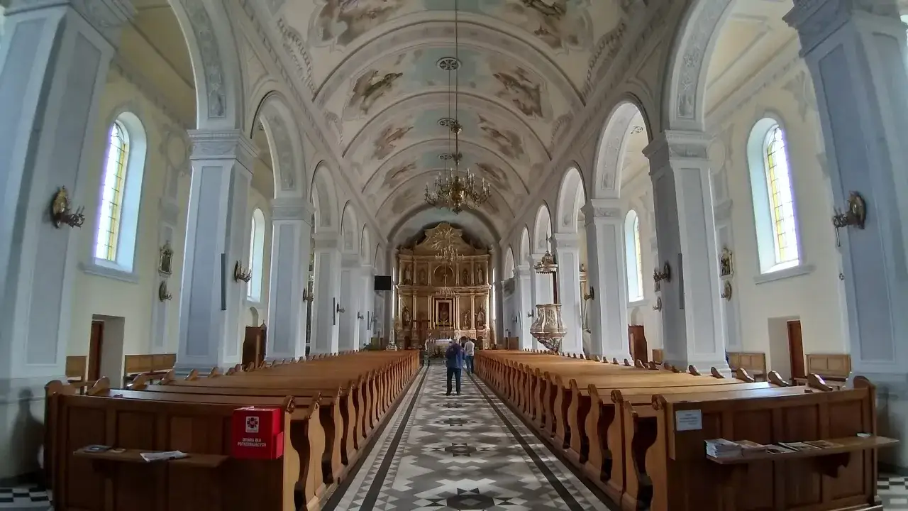 Wnętrze kościoła w Suchanino z malowanym sufitem, rzędami drewnianych ławek i ołtarzem.