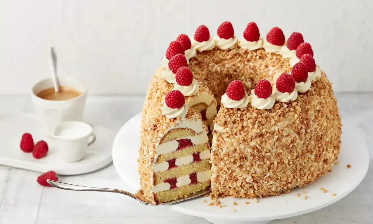 Ein köstlicher Frankfurter Kranz, verziert mit Sahnetuffs und frischen Himbeeren, wartet darauf, angeschnitten zu werden.