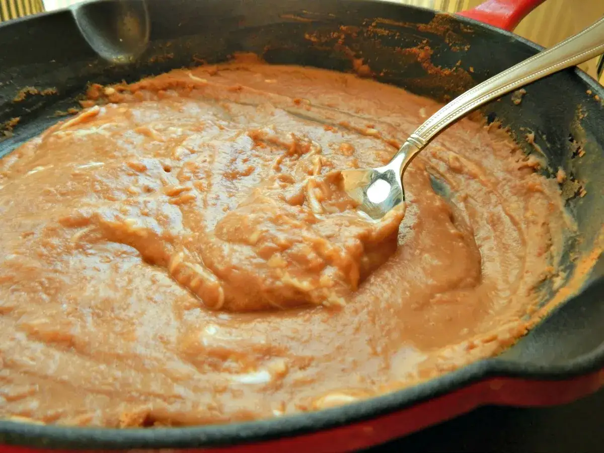 En gjutj&auml;rnspanna med kr&auml;miga refried beans, en sked vilar i den varma b&ouml;nr&ouml;ran.