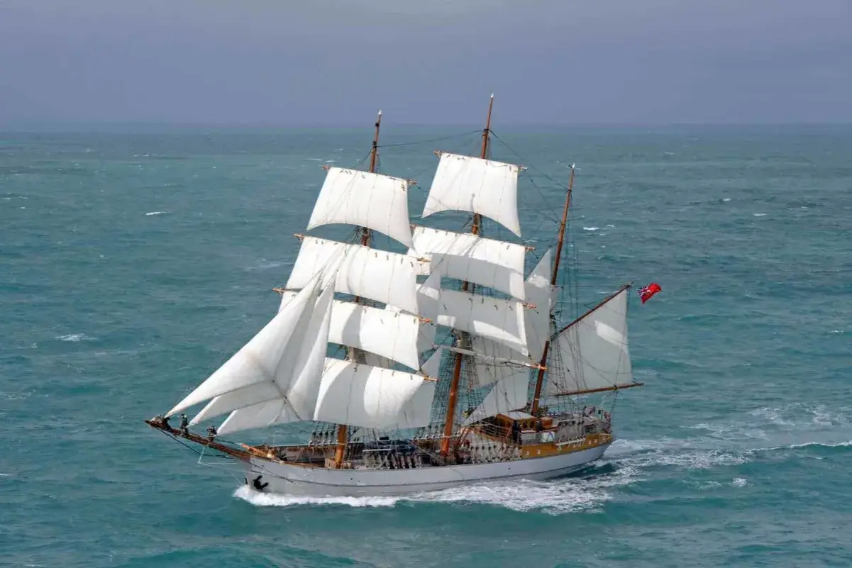 Un majestueux voilier 3 mats fend les vagues bleues, ses voiles blanches gonflées par le vent, prêt pour une grande aventure maritime.