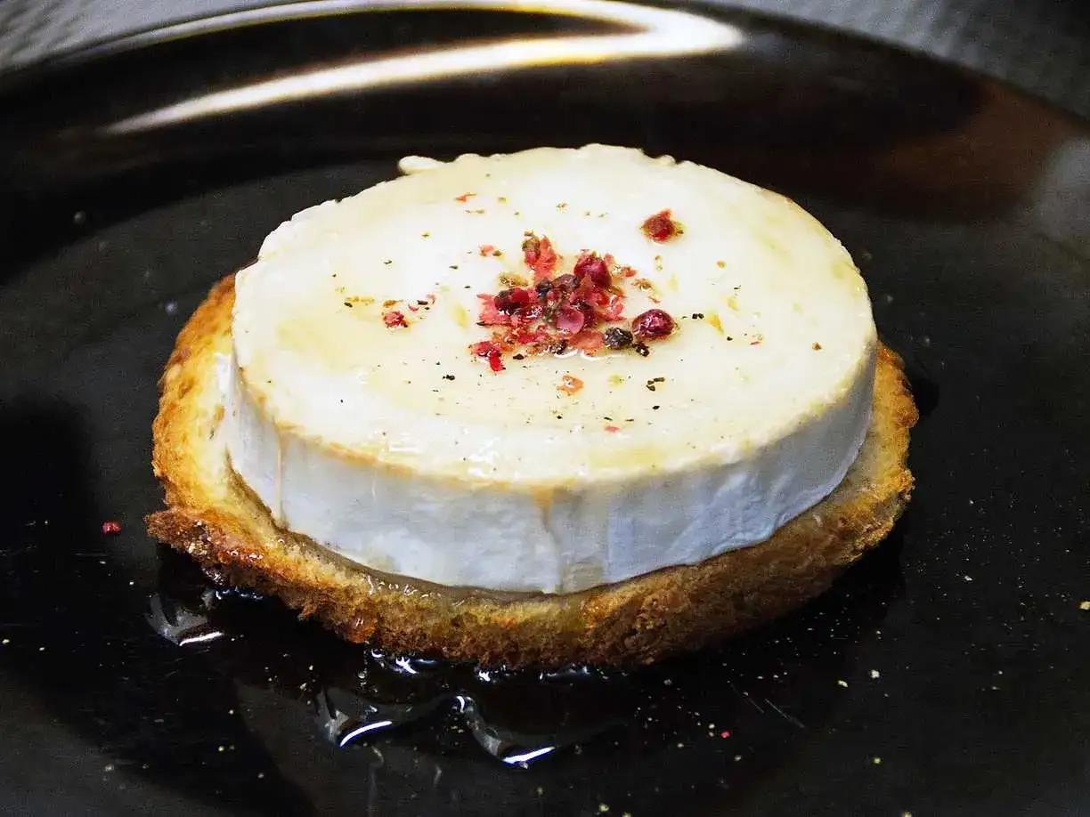 En rostad brödskiva med smältande chevre chaud, toppad med peppar och rosa bär.