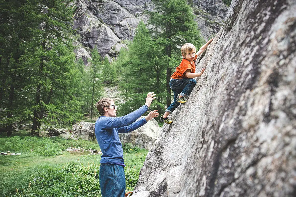 Un père encourage son fils à faire de l'escalade sur un rocher, entourés par la nature.