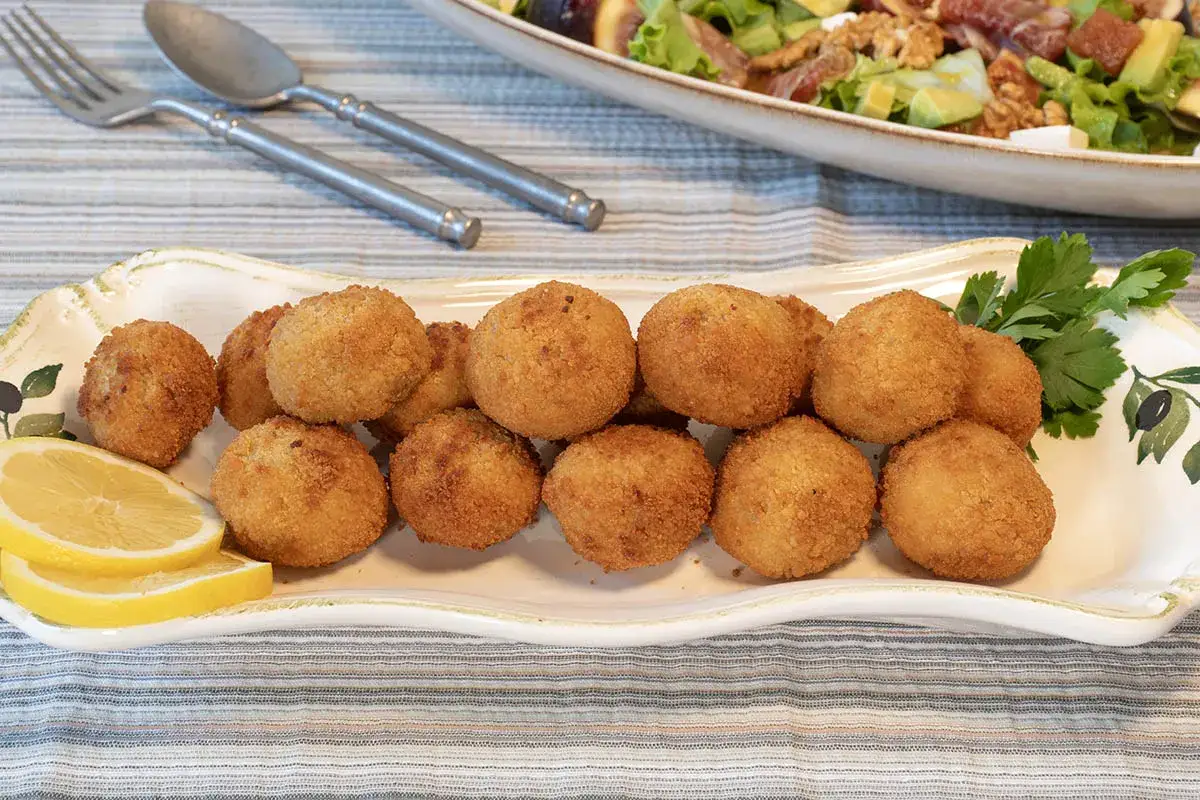 Croquetas de pollo doradas y crujientes en una bandeja decorada, acompañadas de rodajas de limón y perejil.
