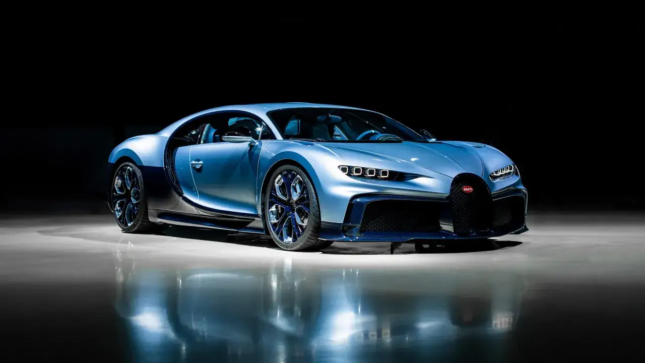 Błękitny Bugatti Chiron błyszczy na ciemnym tle, odbijając się w polerowanej podłodze.