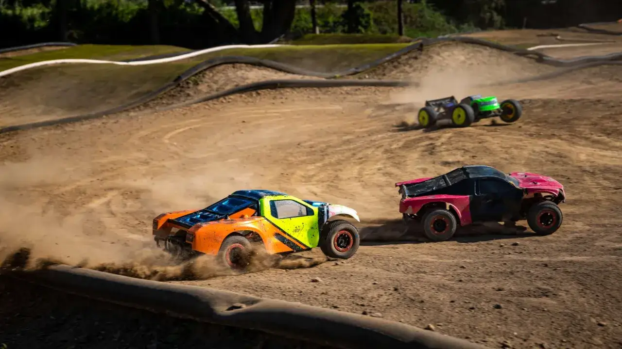 Bunte RC-stadium trucks rasen über eine staubige Rennstrecke, die Reifen wirbeln Erde auf.
