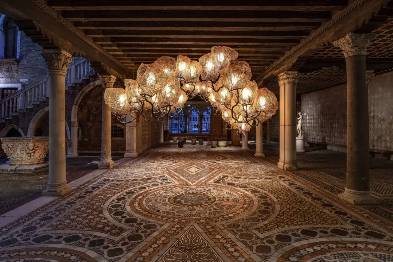 Interni Ca' d'Oro: un lampadario scenografico illumina il cortile con mosaici antichi e colonne imponenti.