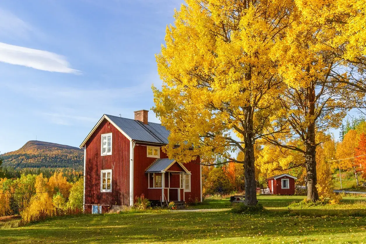 Rotes Haus in Schweden im September. Herbstlaub leuchtet gelb, das Wetter ist sonnig und klar.