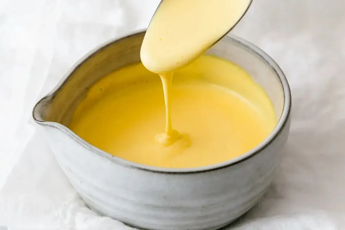 Une cuill&egrave;re verse une sauce hollandaise onctueuse dans un bol en c&eacute;ramique.