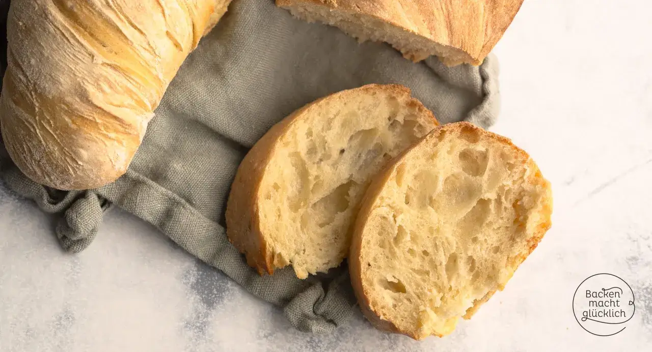 Ein knuspriges Wurzelbrot mit Sauerteig, auf einem Leinentuch angerichtet. Zwei Scheiben zeigen die luftige Krume.