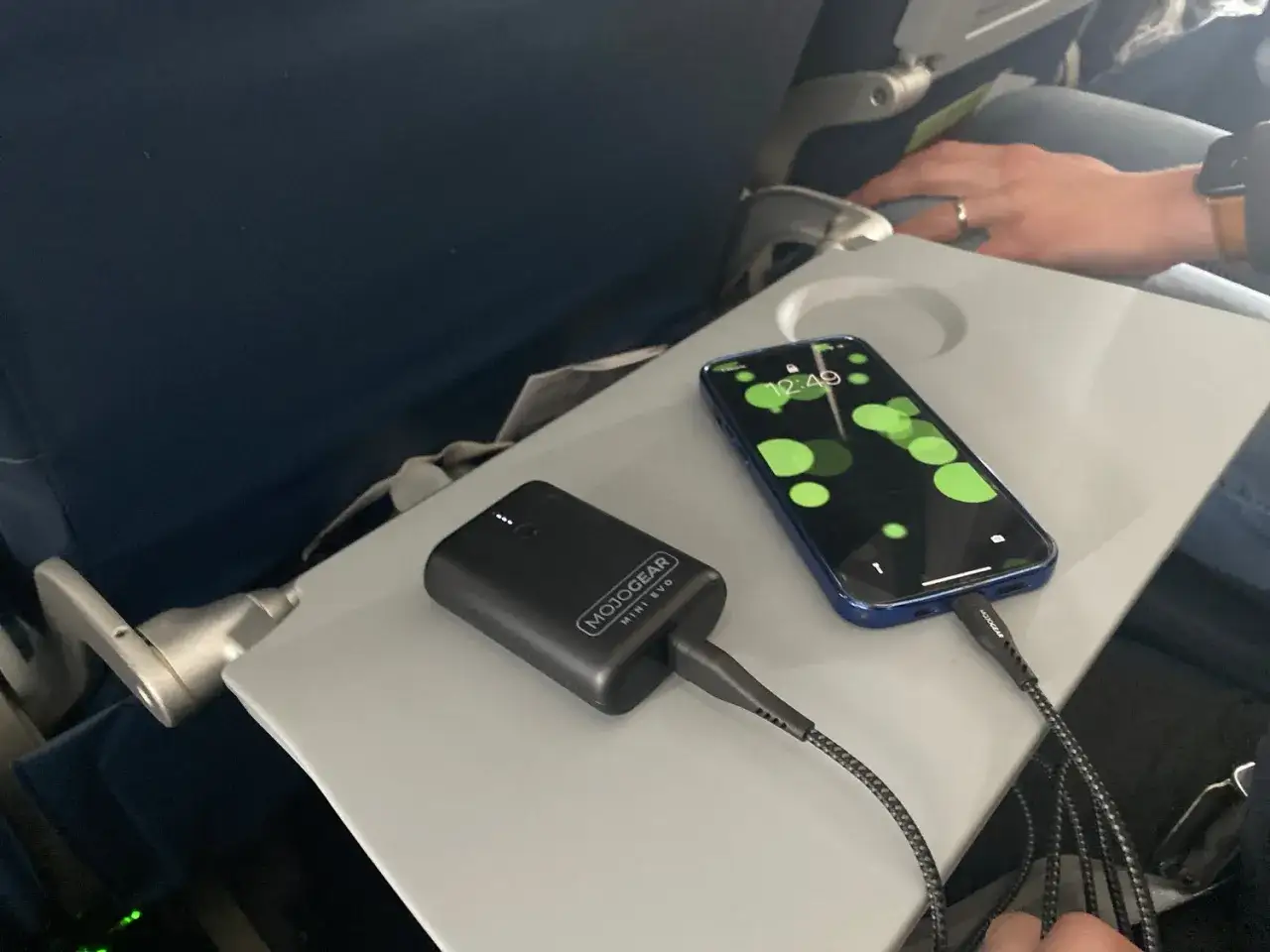 Na stoliku w samolocie ładuje się telefon za pomocą powerbanku w bagażu podręcznym.