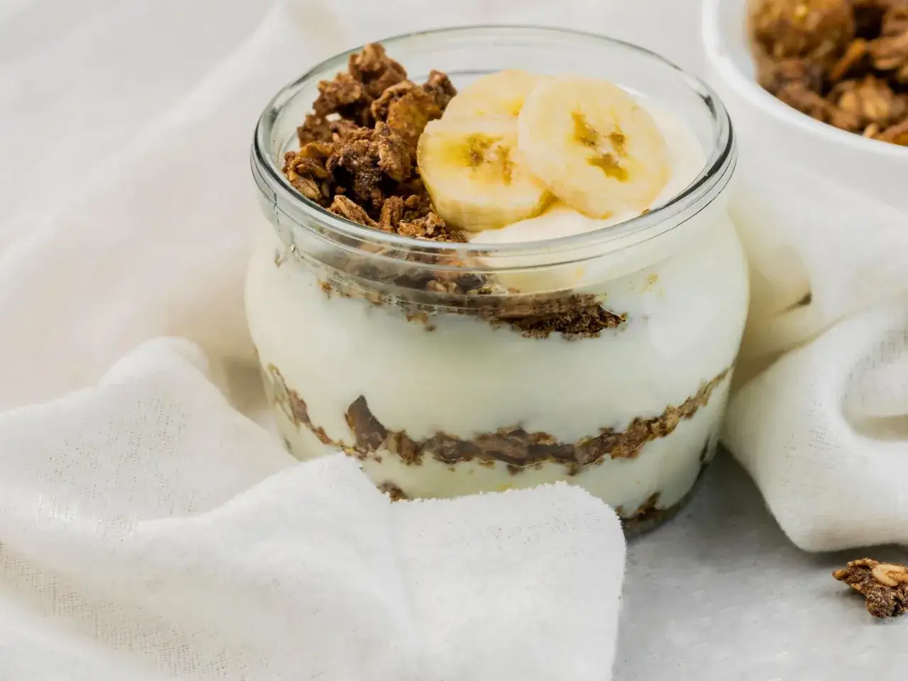 Słoik z jogurtem, granolą i bananem. Alternatywa dla puddingu z tapioki, idealna na śniadanie.