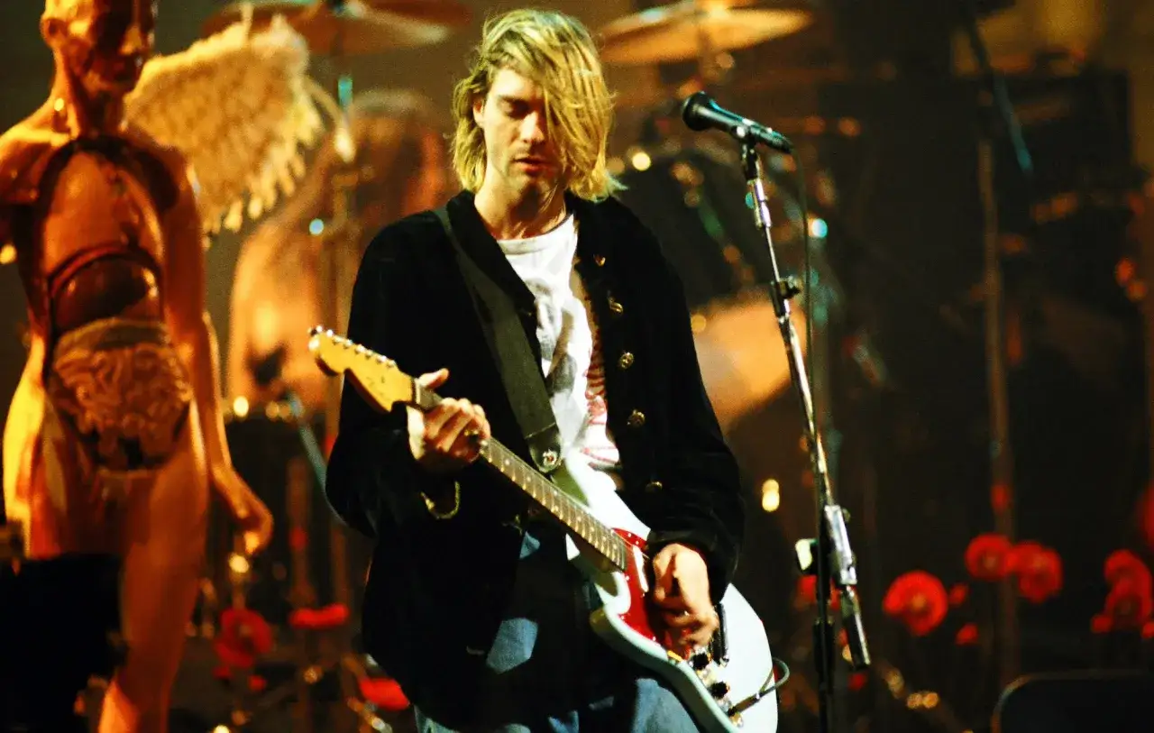 Kurt Cobain z zespołem Nirvana na scenie, grający na gitarze.