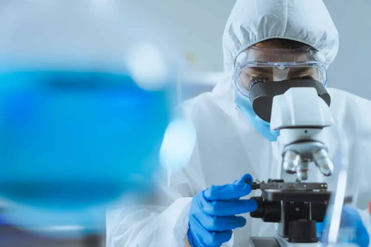 Chercheur en blouse blanche et lunettes examinant une substance bleue au microscope, pour comprendre quelles sont les 5 caractéristiques de l'eau potable.