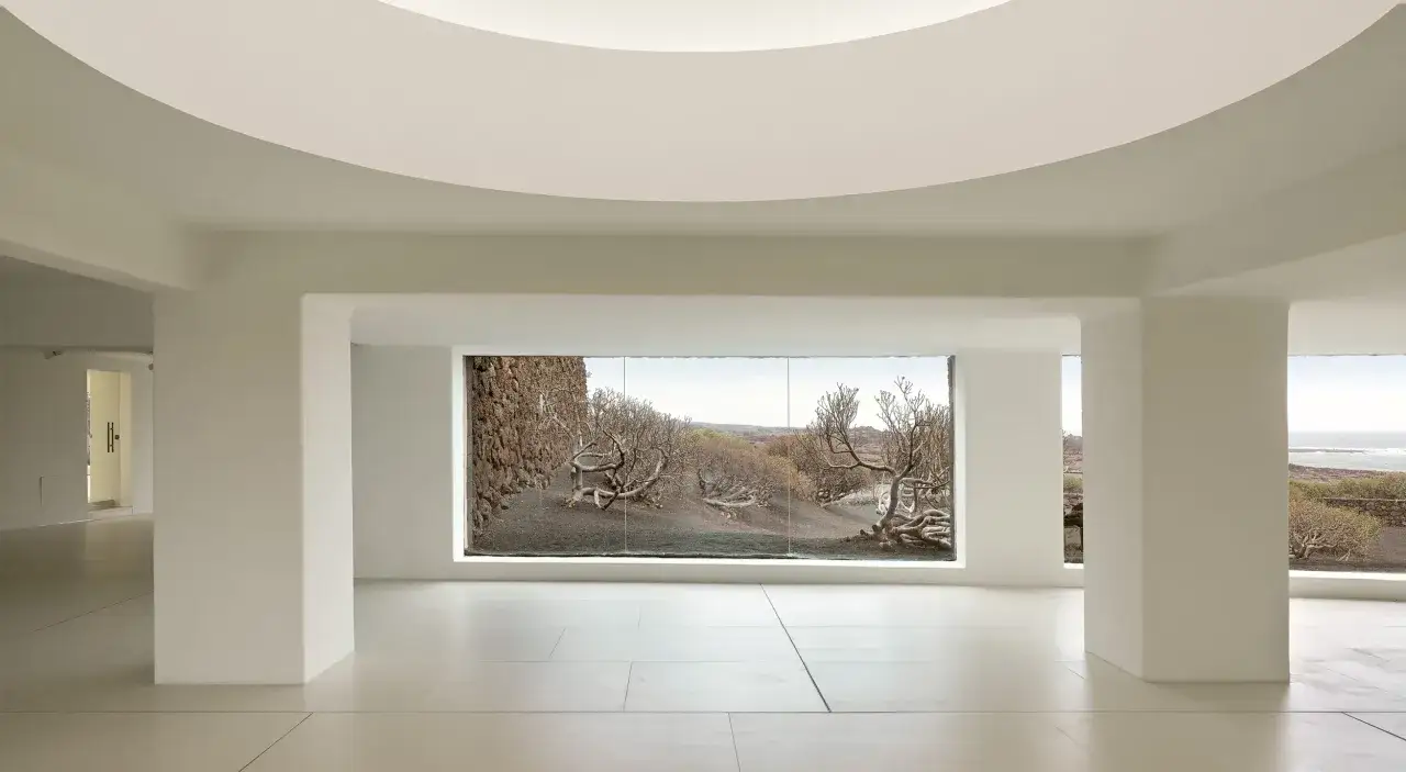 Interior minimalista con vista a un paisaje árido y rocoso, como si fuera la casa de los volcanes.