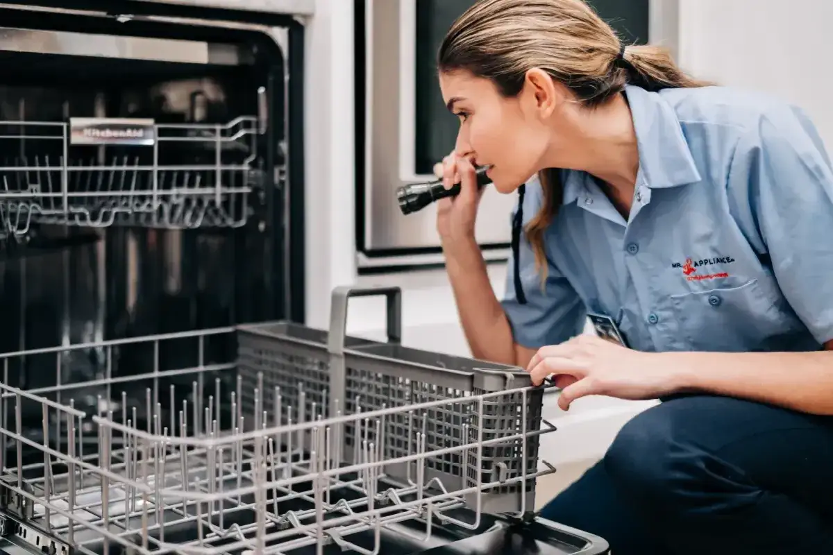 Technik z latarką sprawdza wnętrze zmywarki, przypominając o tym, jak często czyścić zmywarkę, by działała sprawnie.