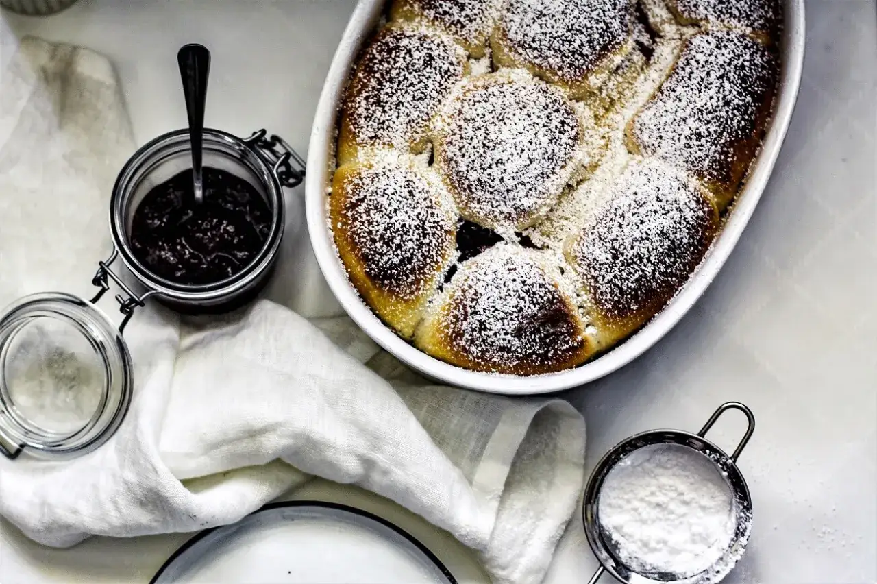 Frisch gebackene Buchty mit Puderzucker best&auml;ubt, daneben ein Glas Marmelade. Ein perfektes Buchty Rezept f&uuml;r s&uuml;&szlig;e Momente.