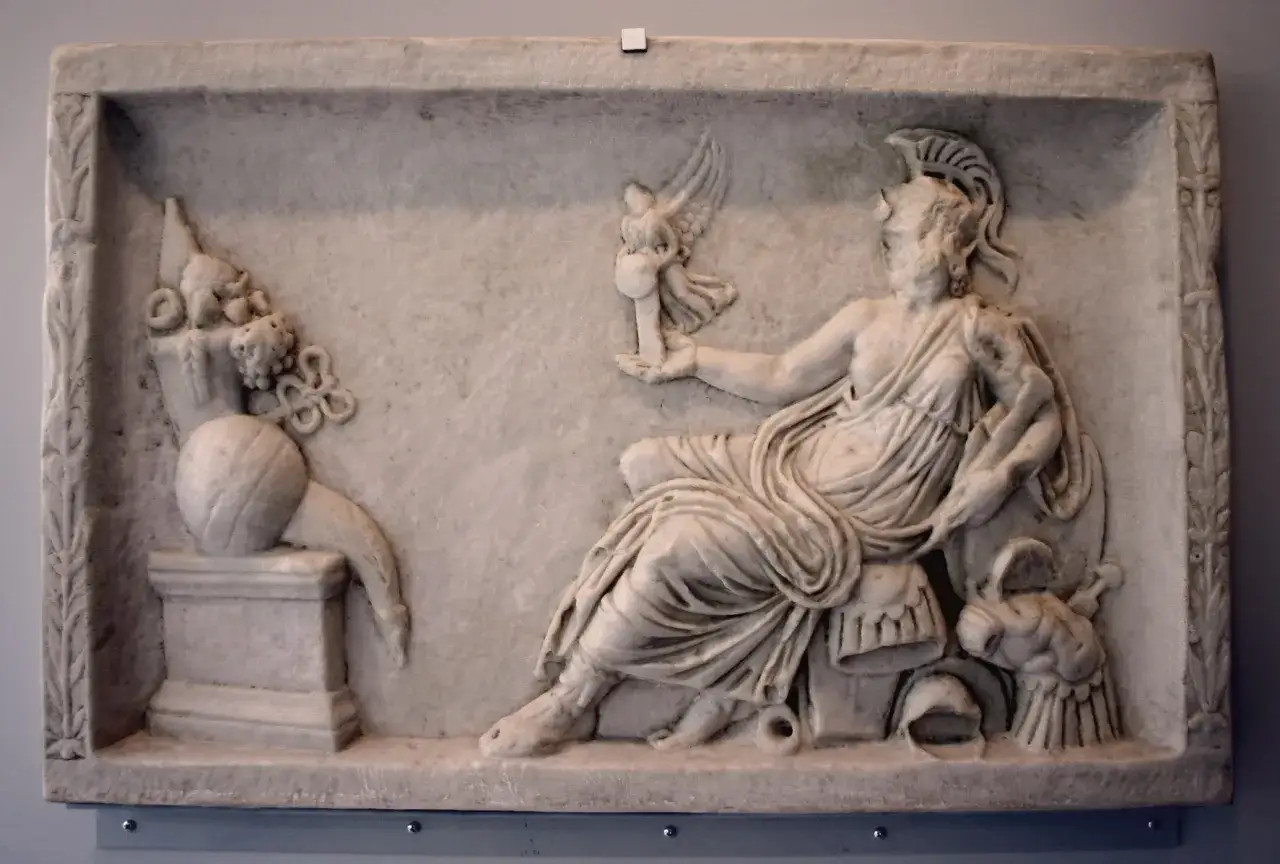 A marble relief depicting a seated figure, possibly a goddess, holding a winged victory. This scene reflects the rich tapestry of Roman paganism, with symbolic offerings and divine representation.