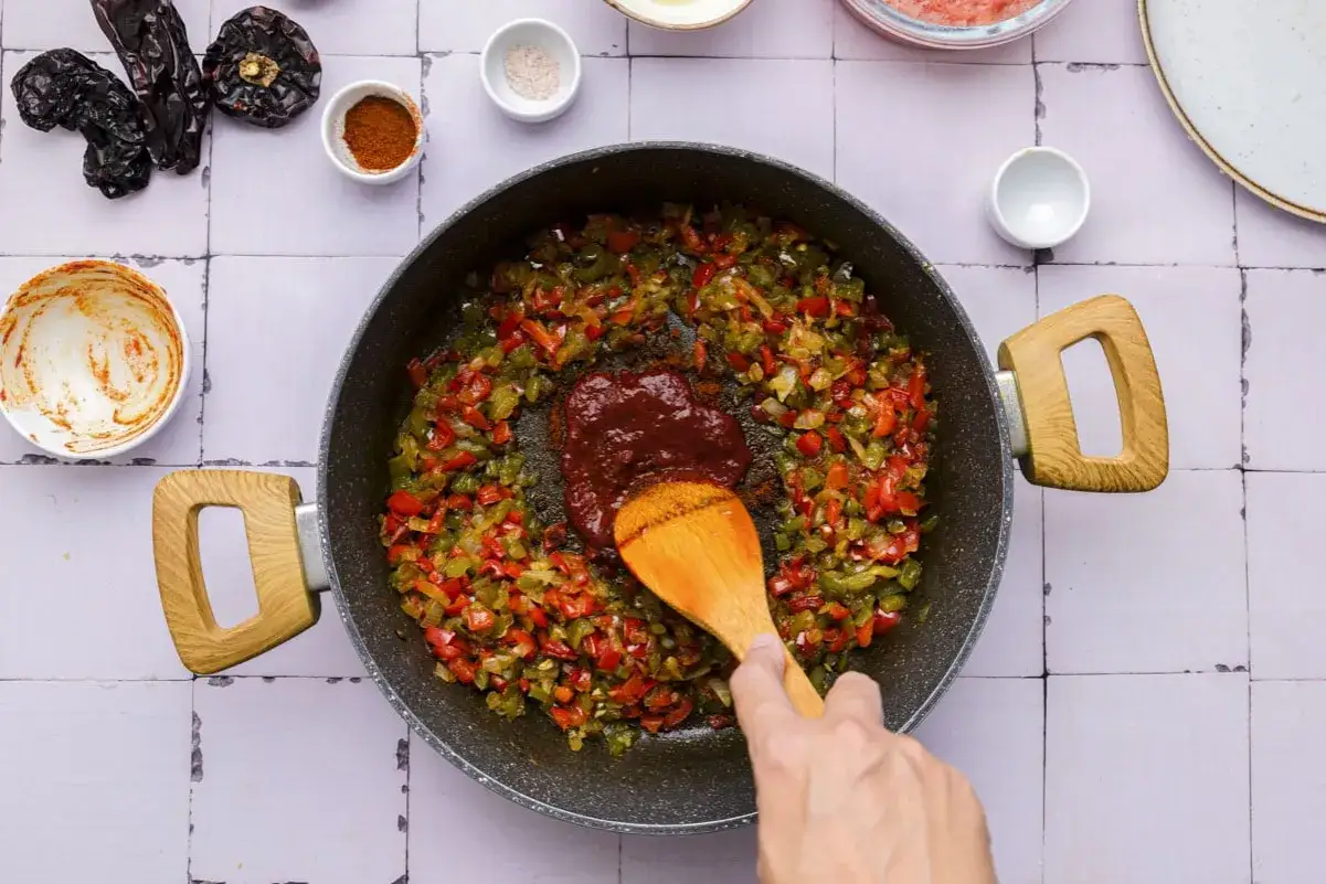 Sofrito, eine Mischung aus gebratenem Gemüse, wird in einer Pfanne mit einer Löffelspachtel vermischt.