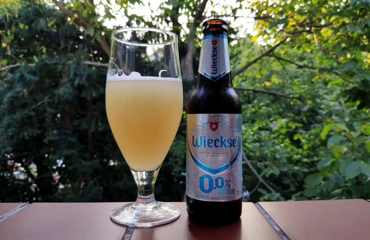 Szklanka i butelka piwa Wieckse 0.0%, holenderska marka piwa, na tle zieleni.