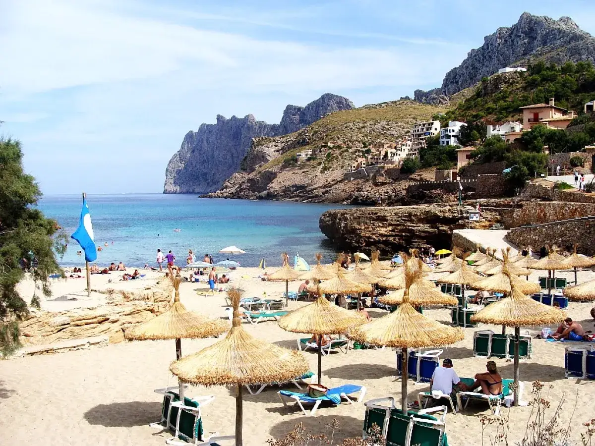 Słoneczna plaża de Formentor z turkusową wodą, g&oacute;rami w tle i licznymi parasolami.