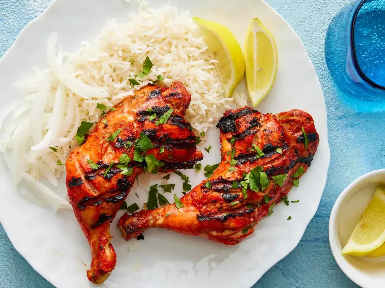 Två saftiga bitar tandoori kyckling med grillränder, serverade med basmatiris, tunt skivad lök och citronskivor.