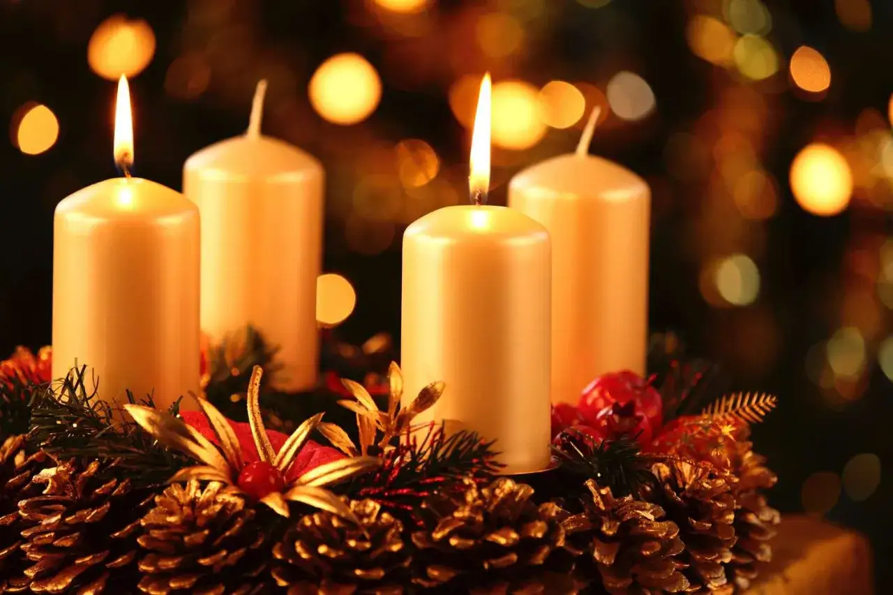 Four lit candles on an advent wreath with pinecones and festive decorations. The second advent is here, bringing warmth and light.