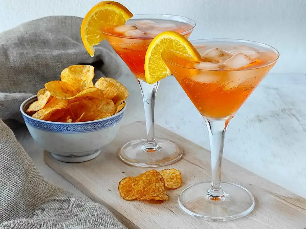 Due bicchieri di Spritz, guarniti con arancia, accompagnati da patatine croccanti. La spritz ricetta perfetta per un aperitivo.