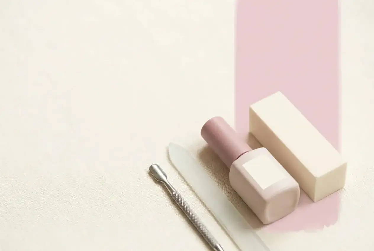 Narzędzia do manicure: pilniczek, metalowy przyrząd, buteleczka z lakierem i blok polerski. Zastanawiasz się, top coat co to? To nabłyszczający lakier nawierzchniowy.