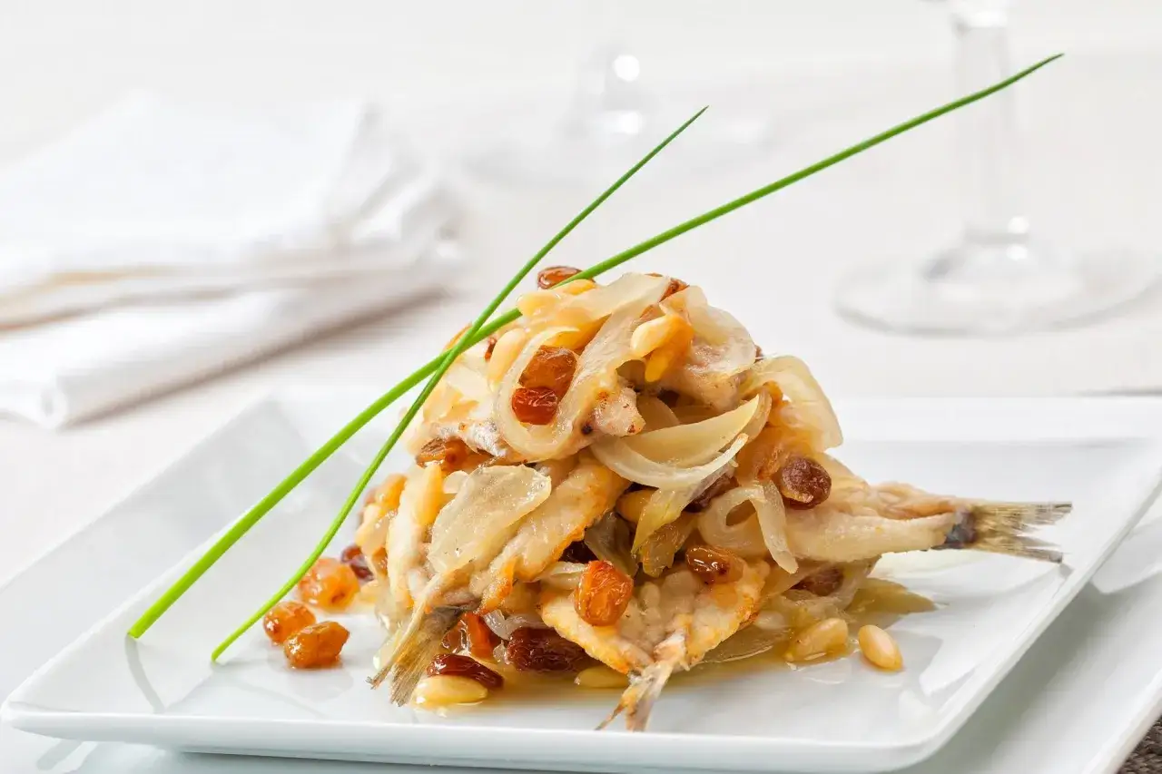 Sardine in saor, un classico dei piatti tipici veneti, con cipolle caramellate, uvetta e pinoli.