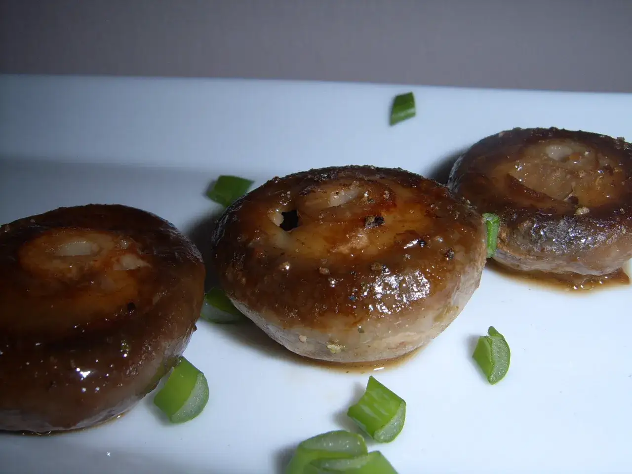 Trzy rumiane pieczarki, idealne do nauki jak usmażyć pieczarki, podane z zieloną cebulką.