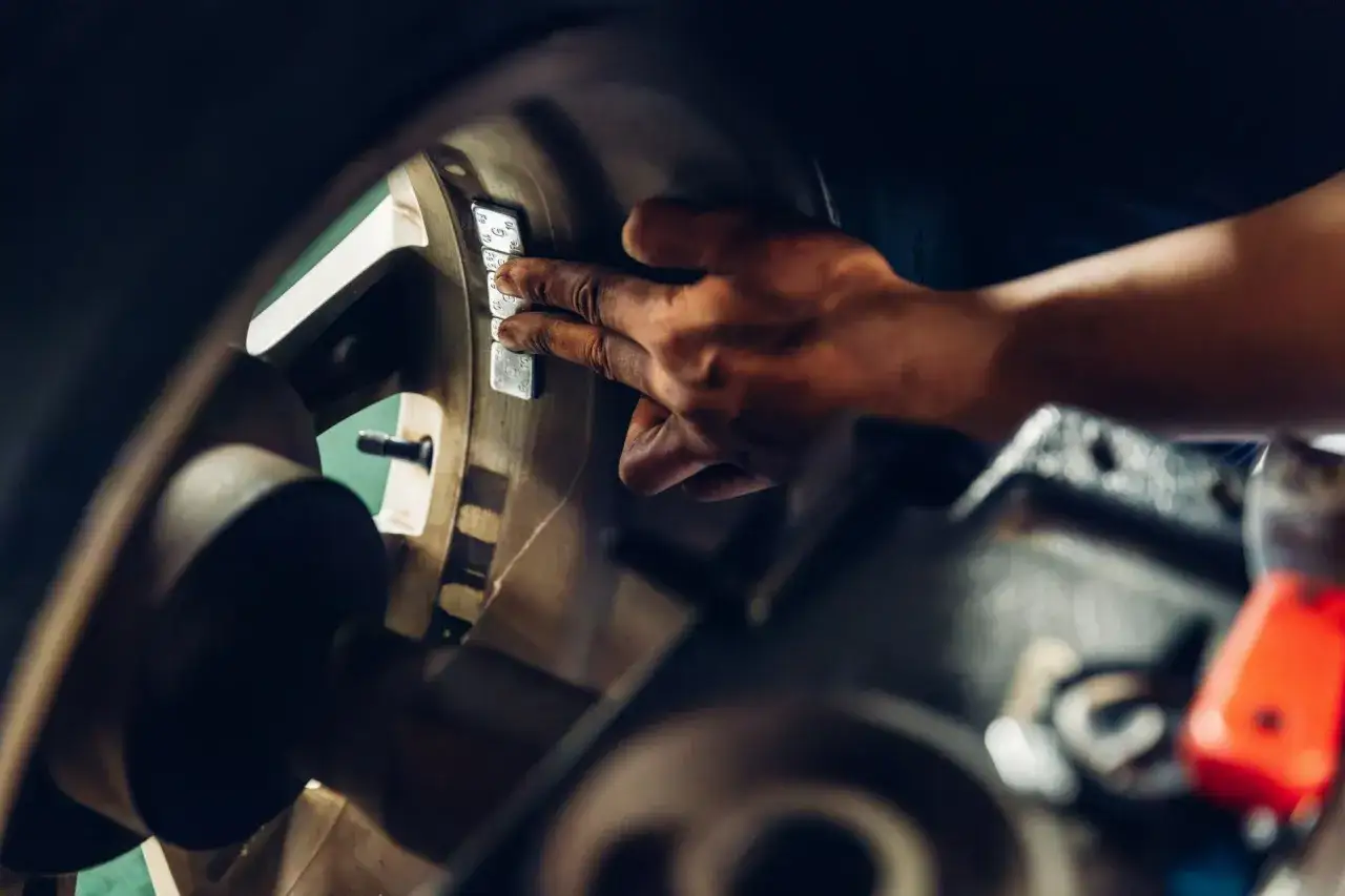 Mechanik przykleja ciężarki do felgi, by zapobiec biciu opony. Objawy nierównomiernego zużycia opon i wibracji kierownicy mogą świadczyć o problemie.