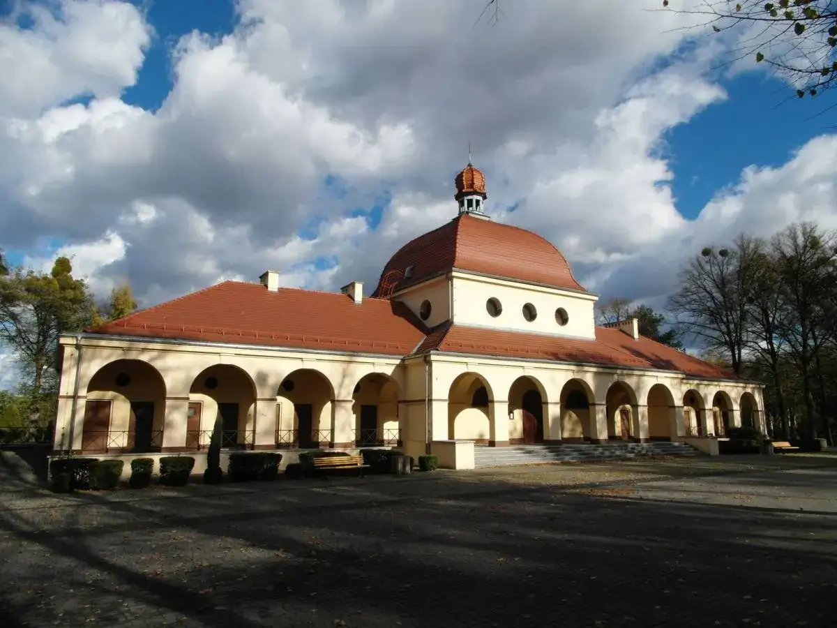 Cmentarz centralny w Gliwicach: krematorium z arkadowym portykiem i kopułą pod błękitnym, chmurnym niebem.