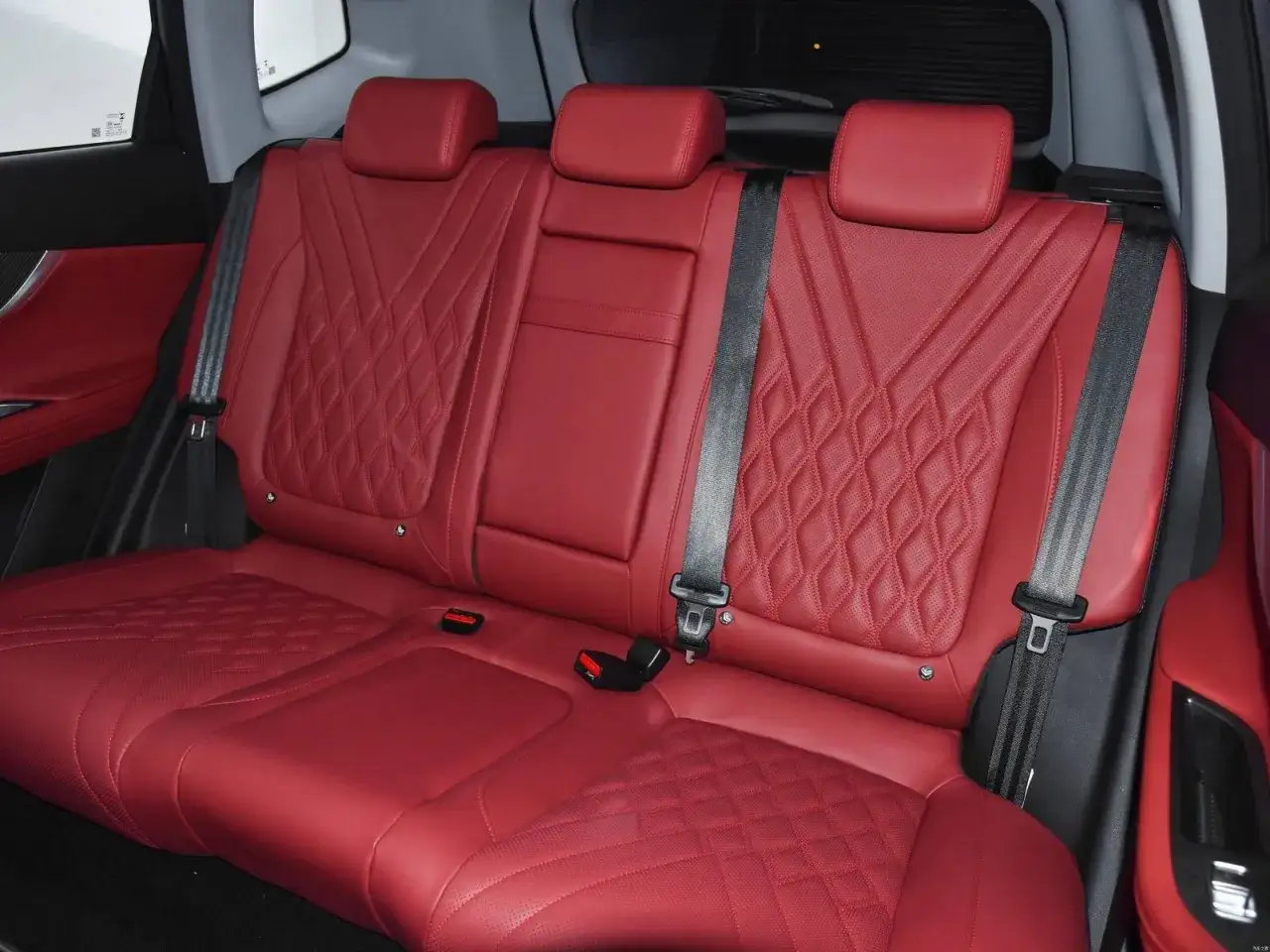 Interno di una chery automobile con sedili posteriori in pelle rossa trapuntata e cinture di sicurezza nere.