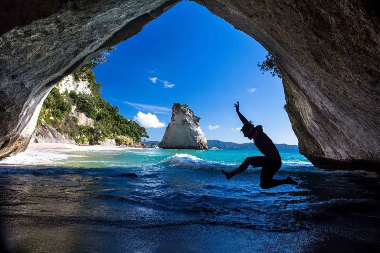 Ein Mann springt von einer Höhle ins Meer. Ein Traum für jedes Neuseeland Auslandsjahr.