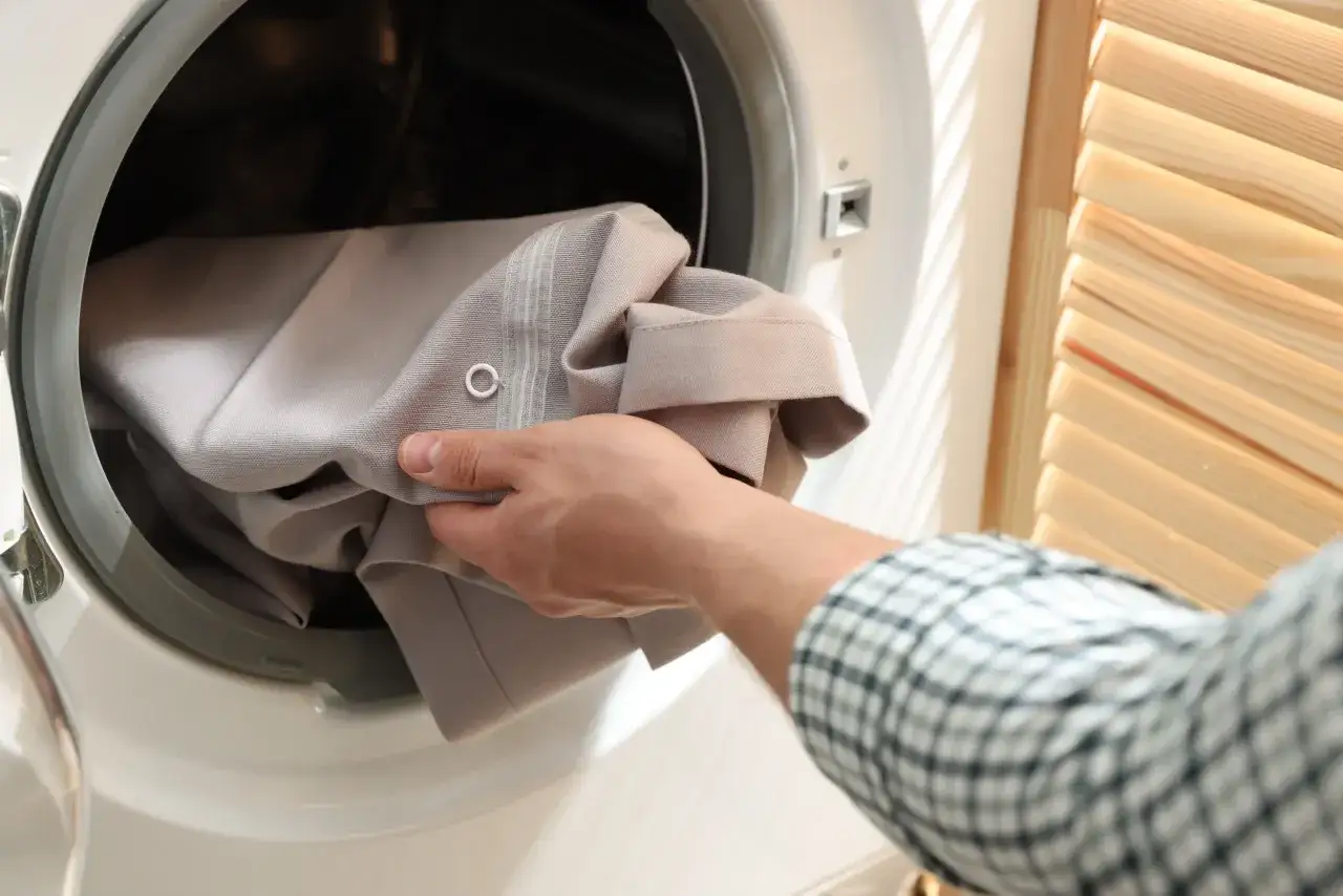 Hand lädt Gardinen in die Waschmaschine. Die Frage