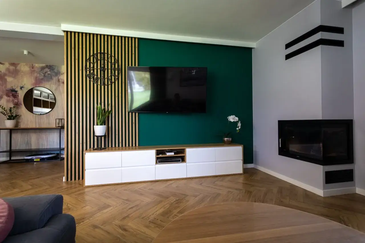 Nowoczesny zielony salon z drewnianą ścianką, telewizorem na ścianie i kominkiem.