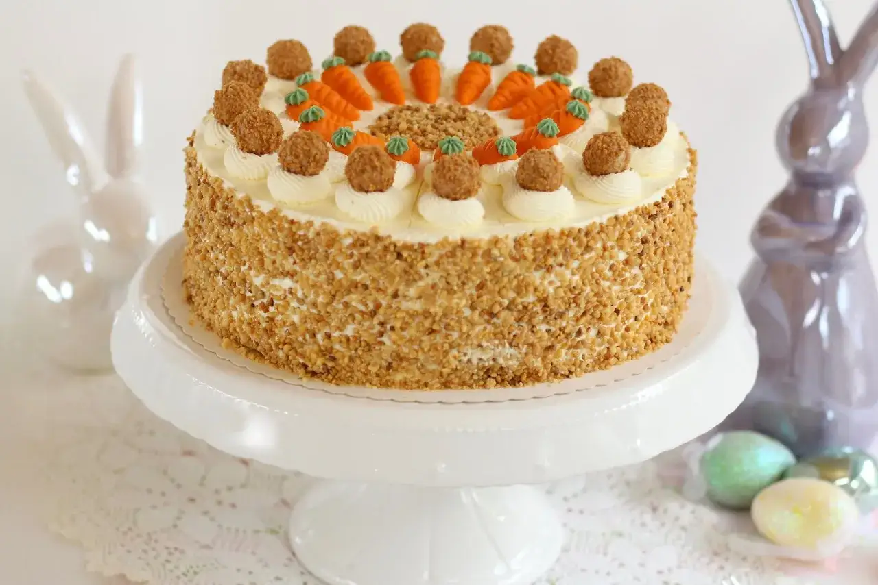 Osterkuchen-Rezepte: Eine Karotten-Torte mit N&uuml;ssen, verziert mit kleinen M&ouml;hren und Pralinen, neben Osterhasen und bunten Eiern.