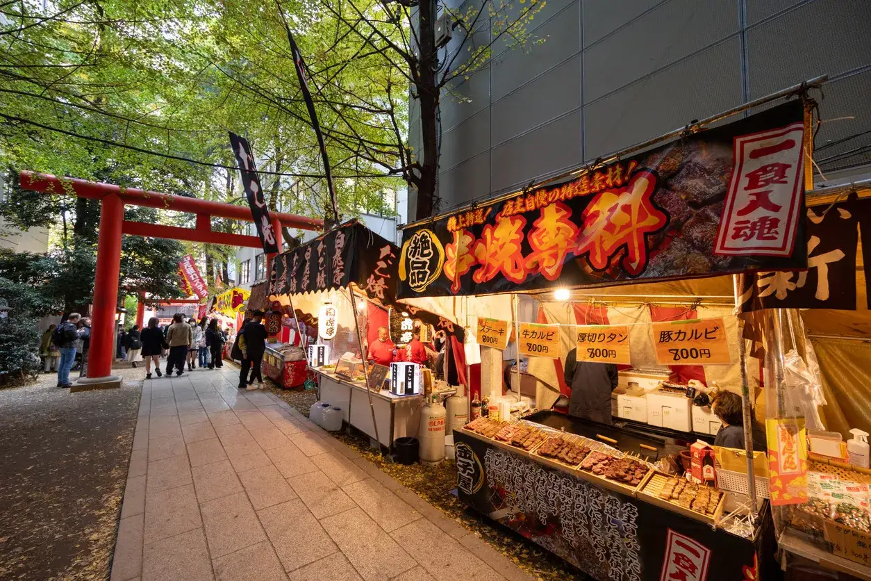 Livlig japansk matmarknad med r&ouml;da portar och st&aring;nd som s&auml;ljer grillspett.