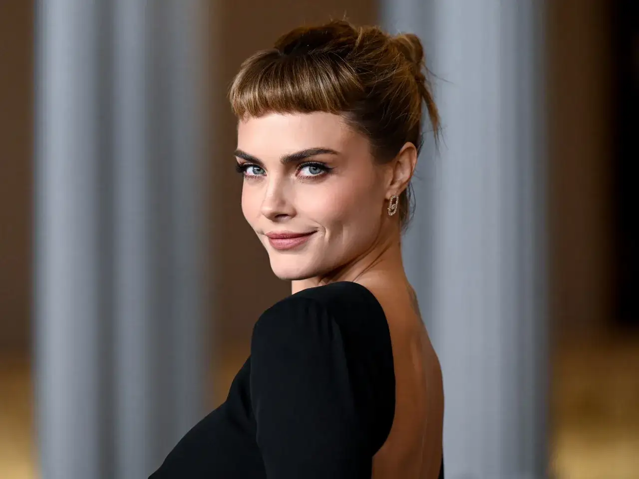 Cara Delevingne, con su distintivo flequillo y mirada penetrante, luce un elegante vestido negro.