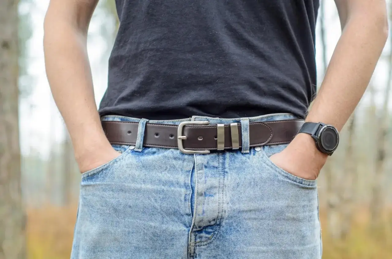 Uomo con jeans chiari e cintura marrone. La fibbia è argentata e si vede da che lato si mette la cintura.