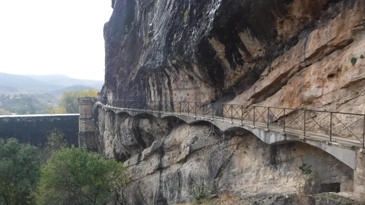 Un pont&oacute;n de la oliva se aferra a un acantilado rocoso, con un camino que serpentea a lo largo de la pared.