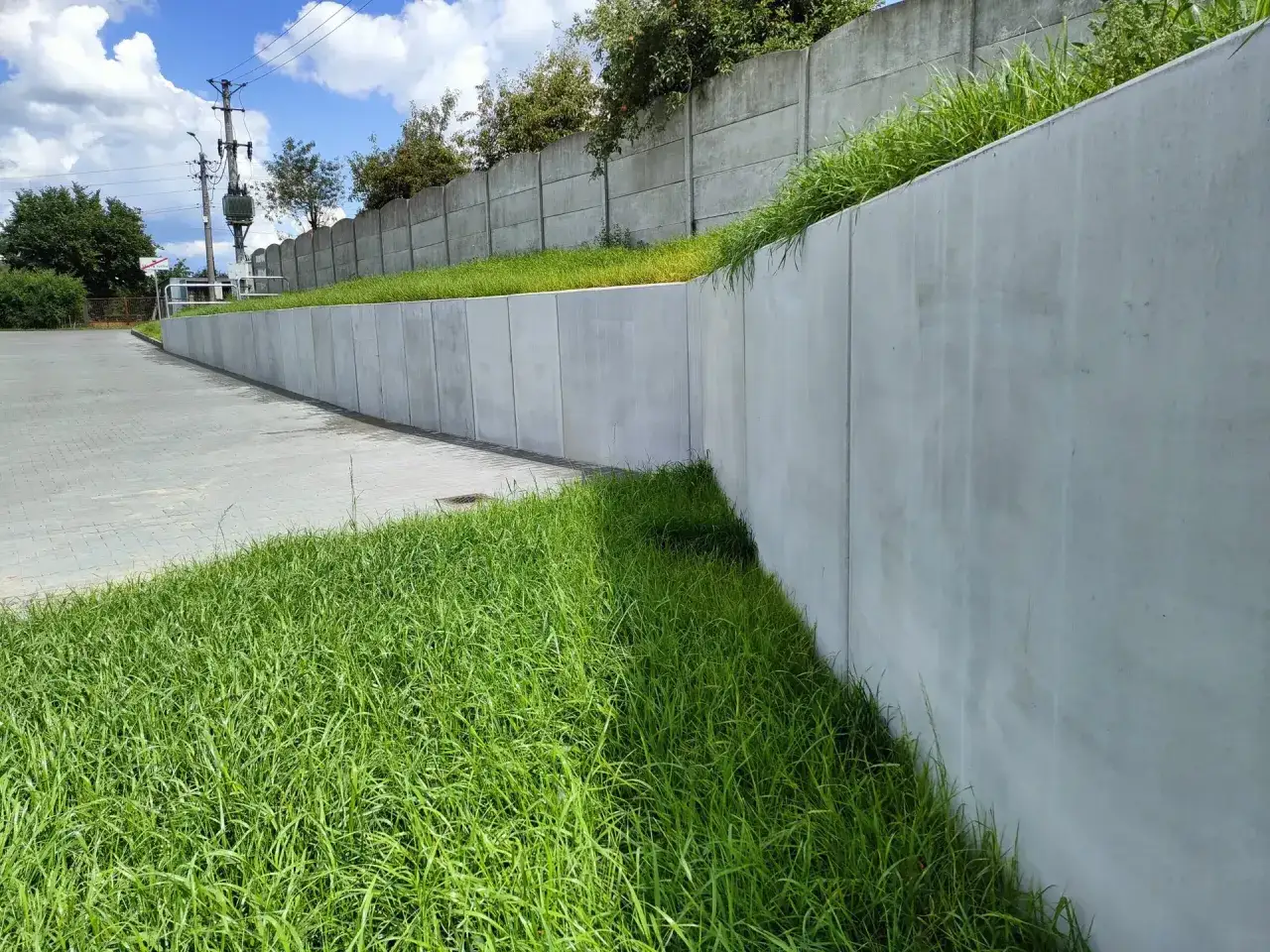 Betonowy mur oporowy, porośnięty trawą, stanowi granicę terenu.