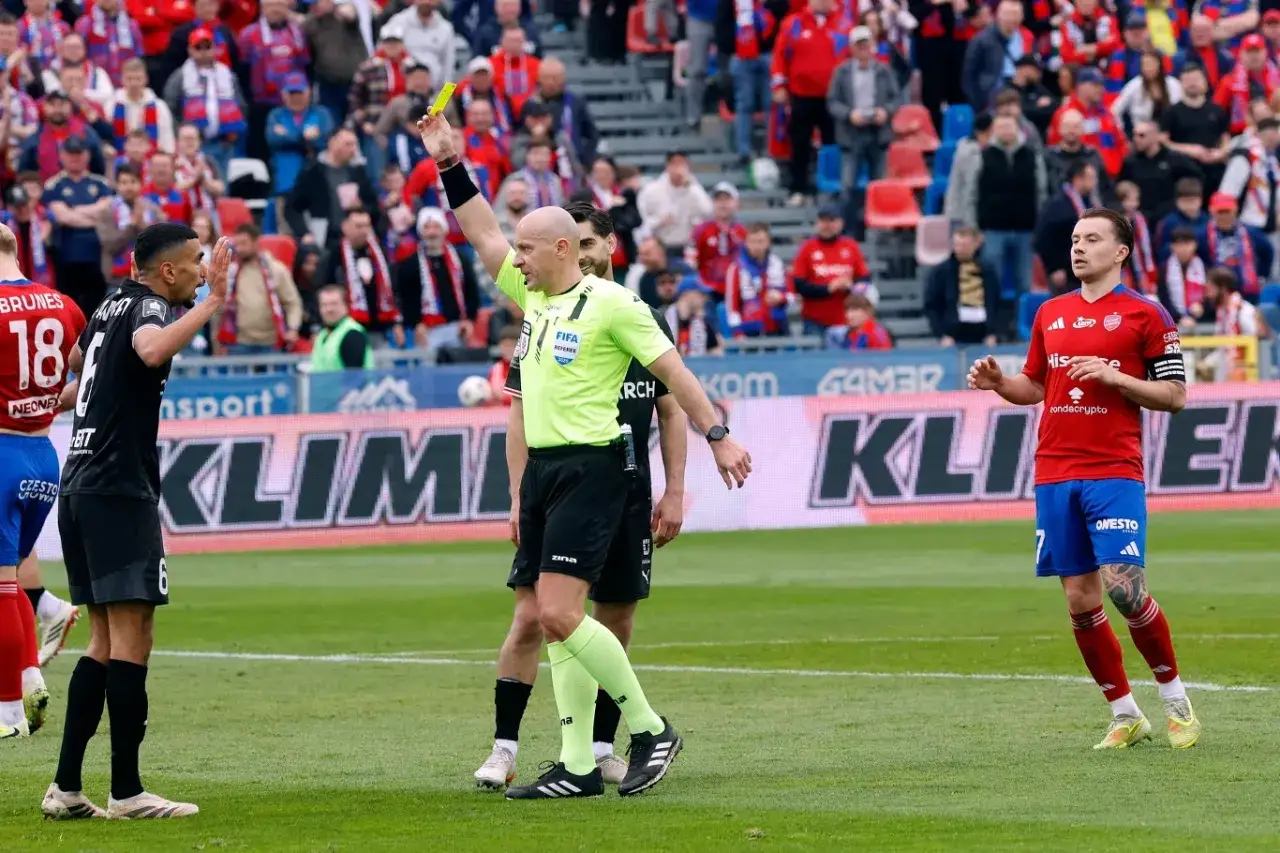 Sędzia pokazuje żółtą kartkę podczas meczu Raków Częstochowa – Cracovia. Piłkarze i kibice na trybunach.