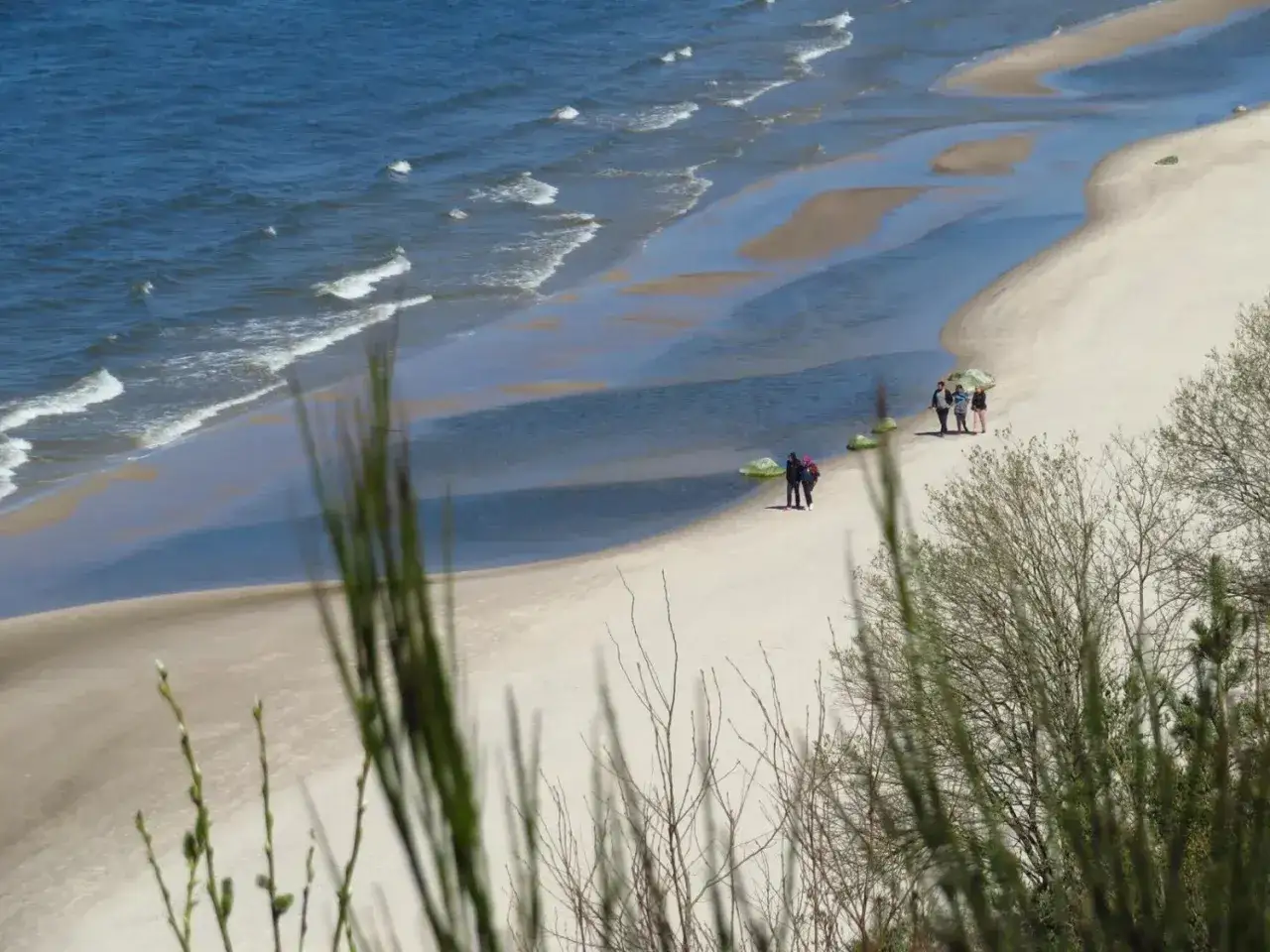 Plaża w Dębinie oferuje piękne widoki i spokojne spacery. Kilka osób spaceruje po piaszczystym brzegu, ciesząc się widokiem morza.