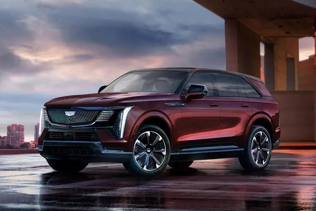 Der Cadillac Escalade IQ in tiefem Rot steht auf nasser Stra&szlig;e vor einer modernen Architekturkulisse.