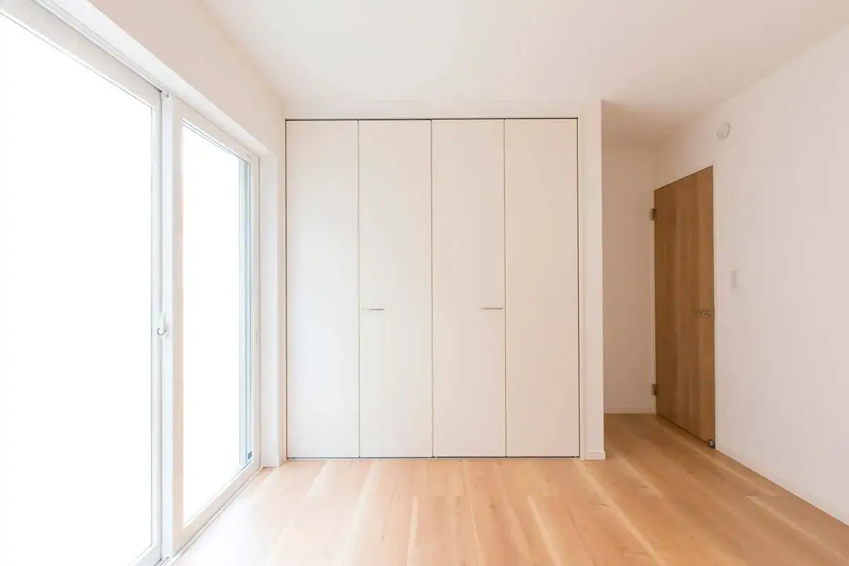 Amplia habitaci&oacute;n con suelo de madera clara y grandes ventanales. En la pared principal, se integran discretamente armarios ocultos en pared, ofreciendo un dise&ntilde;o minimalista y funcional.