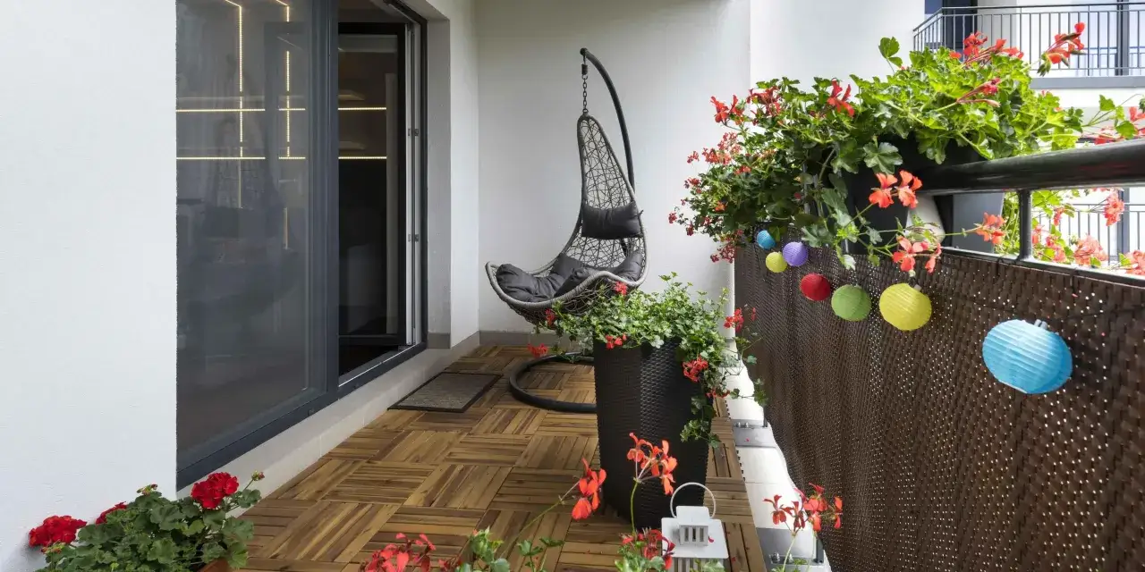 Un balcone accogliente con pavimento in legno, ideale per un progetto di rivestire pavimento balcone fai da te. Sedia sospesa e fiori rossi creano un'atmosfera rilassante.