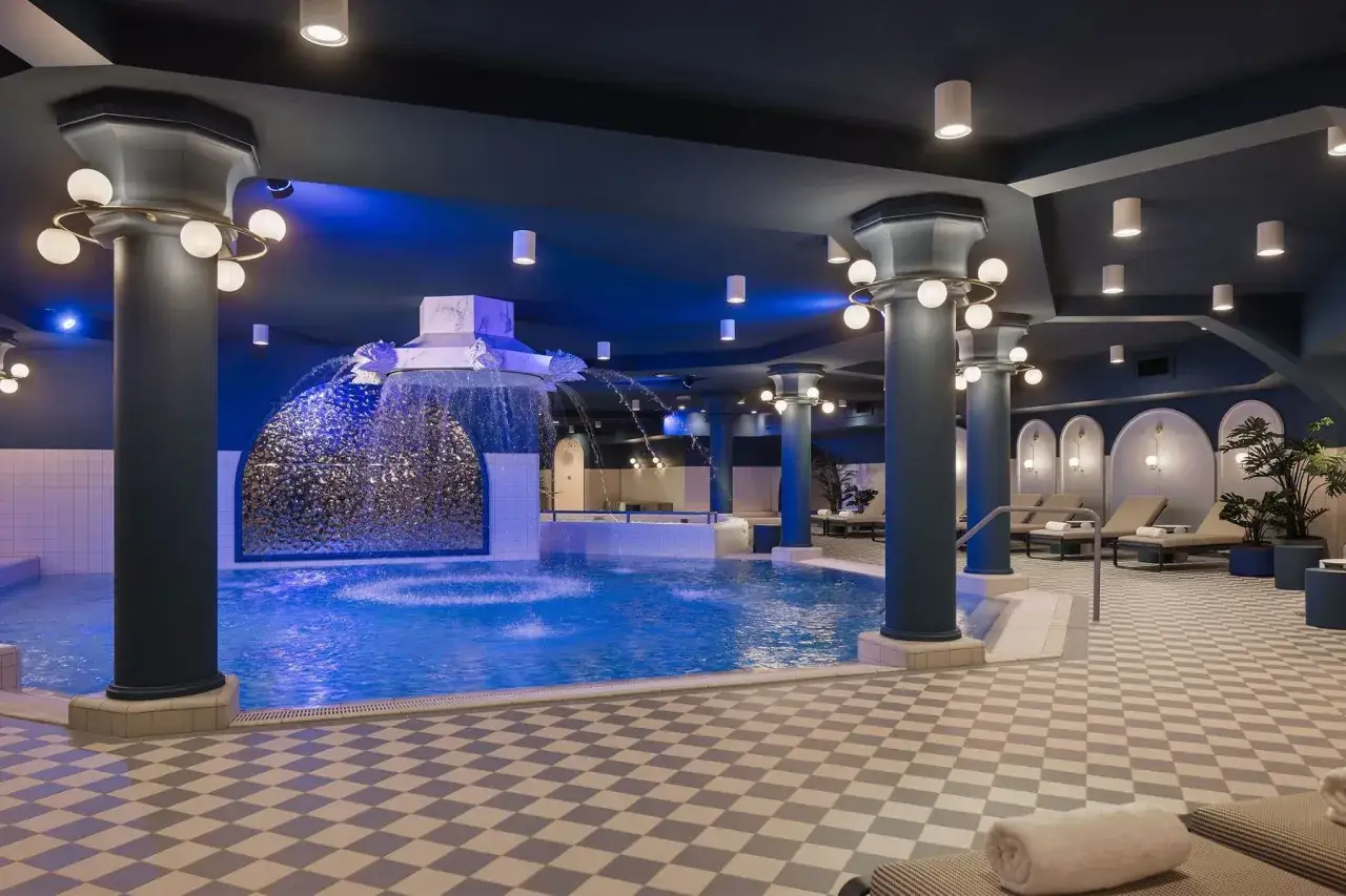 Ein luxuri&ouml;ses **Efteling Schwimmbad** mit blauer Beleuchtung, einem Wasserfall und Liegest&uuml;hlen.