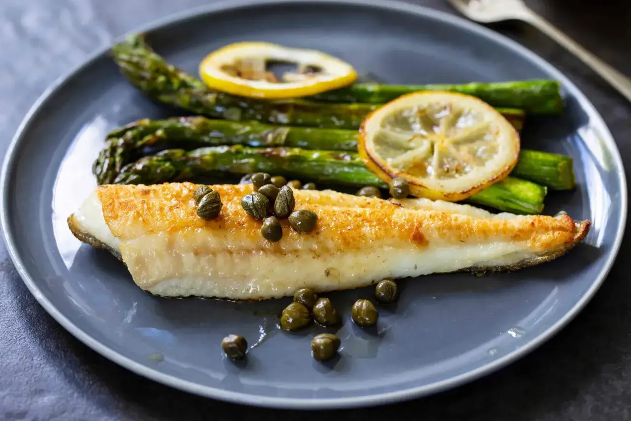 Sogliola in friggitrice ad aria, croccante e dorata, servita con asparagi verdi, capperi e fette di limone.