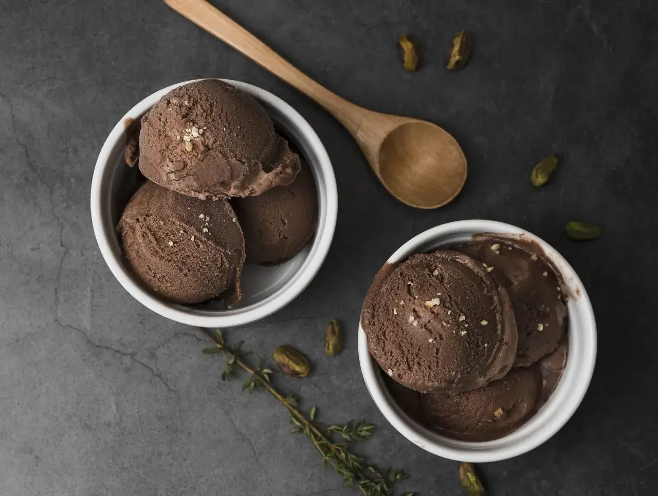 Due ciotole di cremoso gelato alla nutella fatto in casa, guarnito con granella e accompagnato da pistacchi e un cucchiaio di legno.